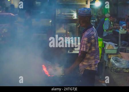 Balikpapan, Indonésie - 15 juin 2024. il est un vendeur de nourriture de rue qui grillent quelques satays pour ses clients. Banque D'Images