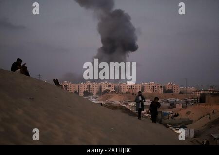 De la fumée s'élève à proximité de la zone des tours Hamad, à l'Ouest de Khan Younis, voyage à Gaza, 14 août 2024. Des avions militaires Iraeli ont attaqué la ville de Hamad alors que l'artillerie explosait des bâtiments résidentiels à Khan Younis, dans le sud de la bande de Gaza, après que des dizaines de personnes eurent été tuées dans des attaques à travers le territoire palestinien au cours des 24 heures précédentes. Les États-Unis et Israël envoient des délégations au Qatar pour des pourparlers de cessez-le-feu qui doivent commencer plus tard aujourd’hui, tandis que le Hamas a déclaré aux médiateurs qu’il était prêt à se réunir après les discussions pour déterminer s’il y avait une réponse sérieuse d’Israël aux propositions de trêve. Photo de Ramez Habboub/ Banque D'Images