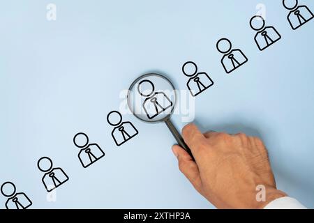 Une main tenant une loupe se concentre sur une icône de personne unique dans une rangée d'icônes de personne. Concept de recherche ou de recrutement de talents. Banque D'Images