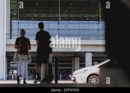 Schoenefeld, Deutschland. 12 août 2024. Deux voyageurs se tiennent devant le bâtiment de l'aéroport de Berlin-Brandebourg 'Willy Brandt' (BER) à Schoenefeld, le 12 août 2024. Crédit : dpa/Alamy Live News Banque D'Images