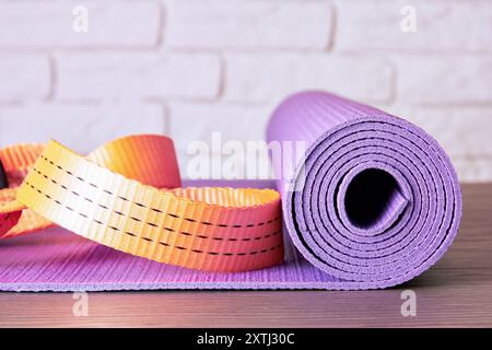 Tapis de yoga violet enroulé sur une surface en bois avec un bracelet orange vif. Thème des activités de fitness Banque D'Images