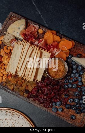 Une planche de charcuterie avec assortiment de fromages, prosciutto, craquelins, fruits secs, bleuets, moutarde, nid d'abeilles Banque D'Images