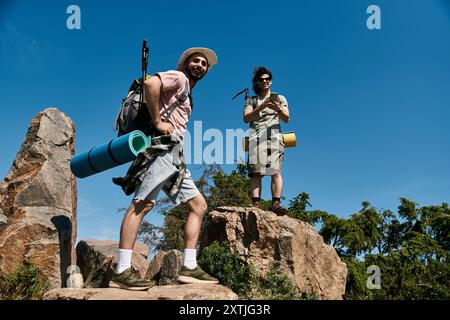 Un couple gay profite d'une randonnée estivale dans la nature sauvage, s'arrêtant pour admirer la vue depuis un sommet rocheux. Banque D'Images