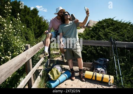 Un jeune couple gay prend un selfie tout en faisant une randonnée dans la nature sauvage estivale, en profitant des beaux paysages et en compagnie les uns des autres. Banque D'Images