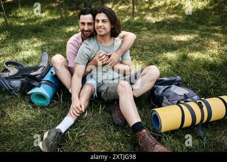 Un jeune couple gay profite d'une randonnée estivale dans la nature sauvage, embrassant et souriant avec amour pendant qu'ils font une pause. Banque D'Images