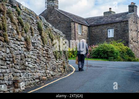 Un vieil homme marchant dans le village de Muker, Swaledale, Yorkshire du Nord Banque D'Images