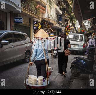 Des femmes vietnamiennes vendant des aliments cuisinés dans la rue de la ville antique. Avec le panier sur son épaule. Vendeuse de nourriture de rue vietnamienne. Voyage Banque D'Images