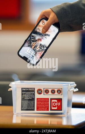 Un étudiant place un téléphone portable dans une boîte avant le début d'un cours au lycée Stonelaw de Rutherglen. La secrétaire à l'éducation, Jenny Gilruth, a visité l'école pour rencontrer les élèves et le personnel scolaire afin de discuter du comportement dans les écoles et de l'impact des téléphones portables dans les salles de classe avant la publication du téléphone portable et de relations plus larges et de conseils comportementaux pour les écoles. Date de la photo : jeudi 15 août 2024. Banque D'Images