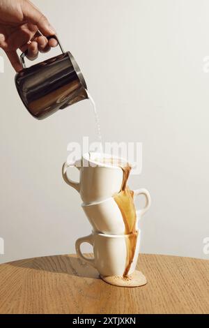 Verser à la main le lait du pichet dans des tasses à café empilées sur une table en bois avec le café qui s'égoutte Banque D'Images