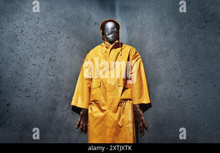 Homme effrayant géant avec ruban adhésif pour le visage enveloppé dans un imperméable jaune vif regardant vers le bas à la caméra debout dans le coin de la pièce. Concept d'horreur Banque D'Images