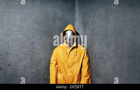 Homme effrayant géant avec ruban adhésif pour le visage enveloppé dans un imperméable jaune vif regardant vers le bas à la caméra debout dans le coin de la pièce. Concept d'horreur Banque D'Images