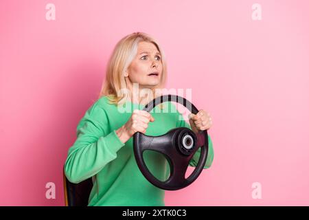 Photo d'une femme retraitée attrayante tenant le conducteur de volant effrayé habillé vêtements verts élégants isolés sur fond de couleur rose Banque D'Images