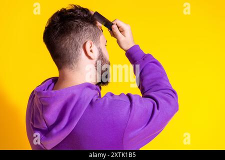 Photo de jeune homme soigné porter des vêtements élégants violets brosse cheveux belle coupe de cheveux isolé sur fond de couleur jaune Banque D'Images