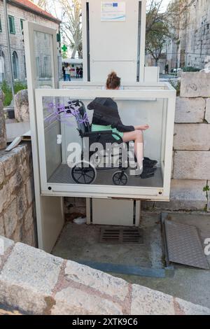 Enfant adolescent fille / fille enfant âgé de 14 ans assis dans un fauteuil roulant, en utilisant l'ascenseur extérieur pour les personnes handicapées dans la vieille ville historique de Split, Croatie. (138) Banque D'Images