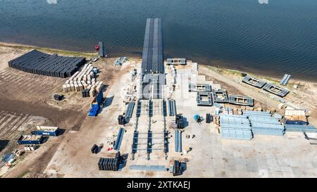 15 août 2024, Brandebourg, Neuendorf : des modules solaires pour le système photovoltaïque flottant sont montés sur des corps flottants sur un chantier de construction sur la mer Baltique de Cottbus (vue aérienne avec un drone). Une fois terminé, le système couvrira 18 hectares du lac (environ un pour cent) avec 51 000 modules solaires. En moyenne, le système peut générer 290000 mégawattheures d'énergie par an. Les corps flottants avec les modules solaires attachés à eux sont reliés au fond du lac par 34 points d'ancrage de sorte que les fluctuations des niveaux d'eau peuvent être compensées. Photo : Frank Hammerschmidt/dpa Banque D'Images