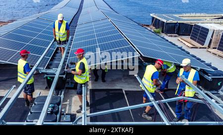 Neuendorf, Allemagne. 15 août 2024. Les travailleurs de la société Pfalzsolar assemblent des modules solaires pour le système photovoltaïque flottant sur la mer Baltique de Cottbus (vue aérienne avec un drone). Une fois terminé, il couvrira 18 hectares du lac (environ un pour cent) avec 51 000 modules solaires. En moyenne, la centrale sera en mesure de générer 290000 mégawattheures d’énergie par an. Les corps flottants avec les modules solaires attachés à eux sont reliés au fond du lac par 34 points d'ancrage de sorte que les fluctuations des niveaux d'eau peuvent être compensées. Crédit : Frank Hammerschmidt/dpa/Alamy Live News Banque D'Images