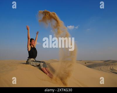 Une fille dans le désert de Dubaï jette du sable et sourit. Banque D'Images