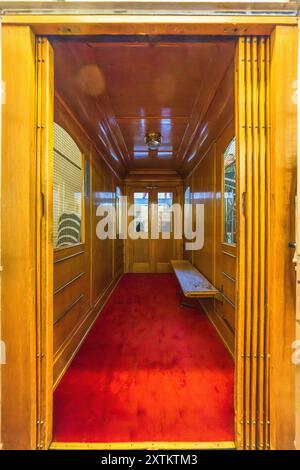 La Schatzalp au-dessus de Davos, Grisons, montre un ascenseur lambré avec un tapis rouge et un banc dans son bâtiment principal. Lorsqu’elle a ouvert ses portes en 1899, la Schatzalp avait déjà des normes sanitaires élevées, un toit plat, un plancher chauffant et cet ascenseur – toutes des particularités pour l’époque. Le grand ascenseur de l’aile principale était suffisamment spacieux pour transporter également les patients tuberculeux décédés : de là, les morts entamaient leur dernier voyage. Otto Pfleghard et Max Haefeli avaient construit le sanatorium pour Willem Jan Holsboer, Bobbahnstrasse, Suisse. Banque D'Images