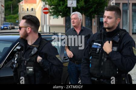 Sebnitz, Allemagne. 15 août 2024. Jürgen Elsässer (M), rédacteur en chef de Compact, entre sur la place du marché avant le début d'un événement de l'AFD, avec des policiers debout devant lui. Le chef de la société de médias d'extrême droite voit la décision de la cour en faveur de son journal comme une victoire contre l'ingérence de l'État. Crédit : Robert Michael/dpa/Alamy Live News Banque D'Images