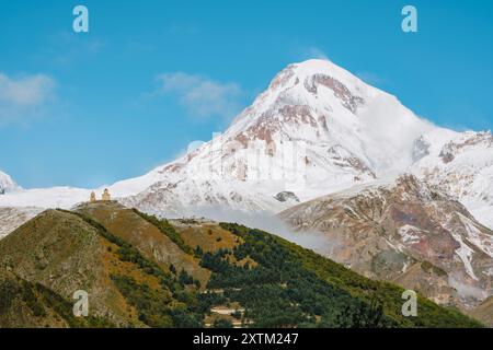 Gergeti Trinity Church perchée sur une colline avec le mont Kazbek enneigé dominant en arrière-plan, sous un ciel bleu vibrant en Géorgie. Banque D'Images