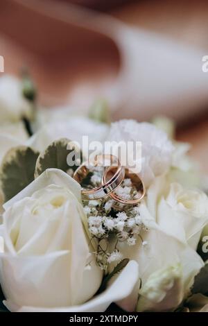 Gros plan des anneaux de mariage sur un bouquet de roses blanches, symbolisant l'amour et l'engagement Banque D'Images