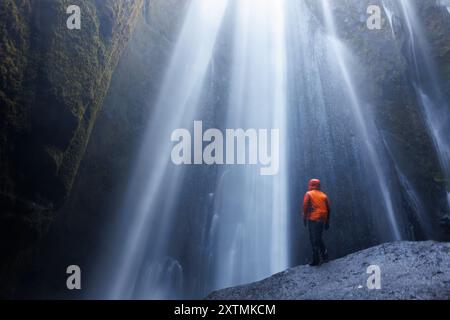 Voyageur à seljalandsfoss cascade posant sous le ruisseau d'eau, la rivière pleut sur les touristes à l'intérieur de la cascade islandaise. Flux froid gelé près des sommets des montagnes et des falaises, paysage majestueux. Banque D'Images