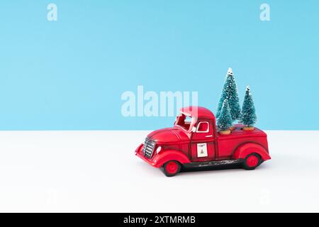 Disposition créative avec camion rétro de Noël rouge et arbres de Noël verts sur fond blanc et bleu clair. Concept minimal de Noël et de nouvel an. Banque D'Images