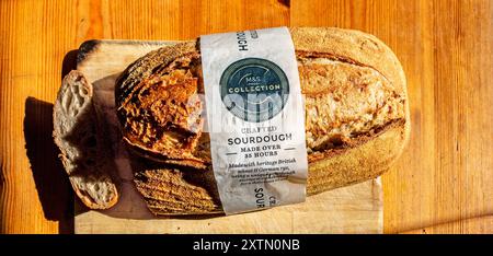 Un pain de levain Crusty Marks and Spencer repose sur une planche de bois, mettant en valeur sa croûte dorée et sa texture. Banque D'Images