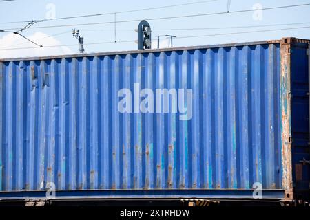 Cette image capture un conteneur bleu chargé dans un train, avec de la rouille et de l'usure qui témoignent de son utilisation intensive dans la logistique mondiale. La suite Banque D'Images