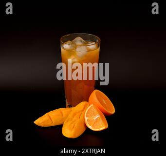 Un grand verre d'un mélange de jus de fruits avec de la glace sur un fond noir, avec des morceaux de mangue mûre et d'orange mélangés. Gros plan. Banque D'Images