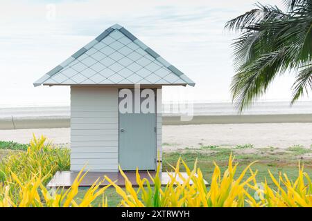 Une cabane solitaire en bord de mer se dresse sur une plage sereine en toile de fond, flanquée d'une végétation tropicale luxuriante et de palmiers, évoquant un sentiment de paix d'isola Banque D'Images