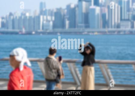 Une image floue de trois personnes sur une promenade au bord de l'eau avec l'horizon de Hong Kong en arrière-plan. Banque D'Images