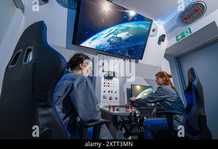 FILED - 15 août 2024, Saxe, Chemnitz : dans le cockpit de la nouvelle capsule spatiale du Centre cosmonaute Sigmund Jähn à Chemnitz, Lena Werner (à gauche) et Zoe Klose manœuvrent dans l'immensité de l'espace. Après une rénovation complète, la capsule spatiale décollera à nouveau avec des vols spatiaux simulés pour les passagers de tous âges pour marquer le 60e anniversaire de l'installation. Samedi (17.08.2024), le Solaris Development Center, sponsor du Cosmonaut Center, organise une célébration d’anniversaire. L'installation pour enfants et jeunes est dédiée aux voyages spatiaux depuis 1964 A. Banque D'Images