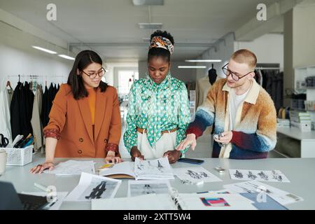 Groupe de jeunes créateurs de mode créatifs discutant de nouveaux croquis de vêtements pour la collection de mode saisonnière par lieu de travail Banque D'Images