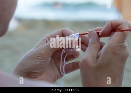 Femme crochette un morceau de fil blanc avec une aiguille rouge sur un fond flou Banque D'Images