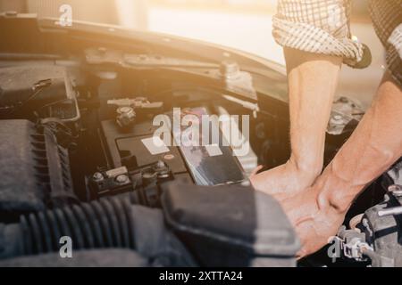 Gros plan des mains de mécanicien automobile vérifiant la batterie d'une voiture. Un homme dévisse un support de batterie automobile. Réparation et remplacement de la batterie. Banque D'Images