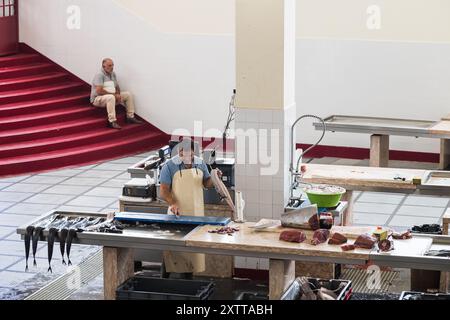 Un homme utilise son couteau pour préparer un poisson noir Scabbard au marché Mercado dos Lavradores à vendre. Photo prise le 6 août 2024 dans le centre de Funchal, Banque D'Images