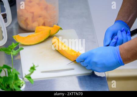 Chef coupant le melon frais sur une planche à découper blanche Banque D'Images