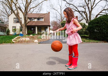 Une petite fille avec des arcs-en-ciel dribble un ballon de basket dans la rue Banque D'Images