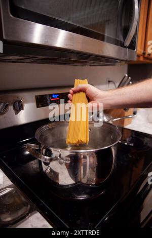 Main tenant des pâtes non cuites au-dessus d'une casserole d'eau bouillante sur une cuisinière Banque D'Images