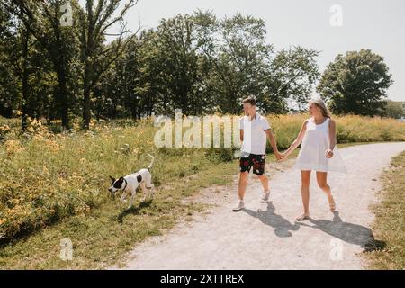 Jeune couple marchant avec un chien sur un chemin bordé de fleurs sauvages Banque D'Images