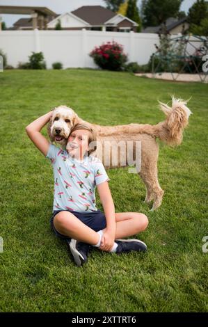 adolescent assis sur l'herbe dans une cour, serrant un gros chien moelleux Banque D'Images