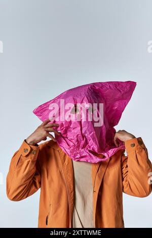 Un homme portant une veste orange vif pose couvert d'un sac en plastique rose. Banque D'Images