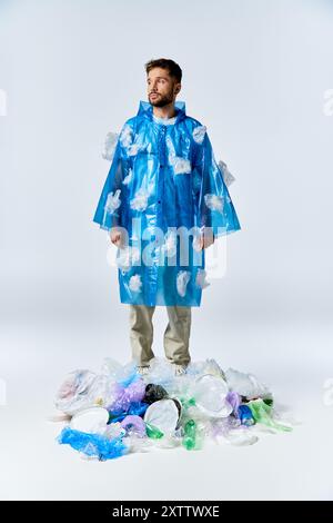 Un homme portant un poncho en plastique bleu se tient sur un gros tas de déchets en plastique. Banque D'Images