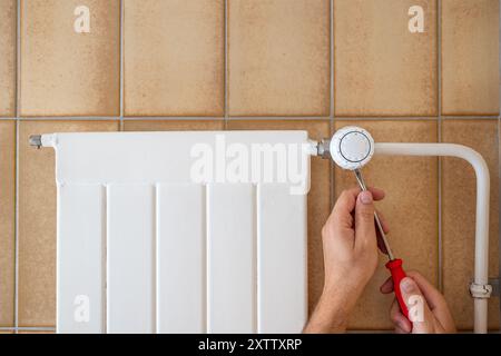 Main masculine caucasienne avec un tournevis fixant le thermostat sur un radiateur domestique. Gros plan, pas de visage, homme méconnaissable. Banque D'Images