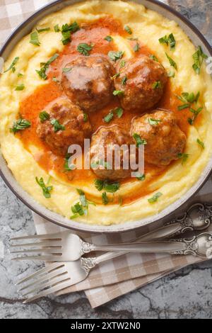 Polenta de maïs à la crème et au fromage servi avec des boulettes de viande dans une sauce épicée gros plan dans un bol sur la table. Vue de dessus verticale Banque D'Images