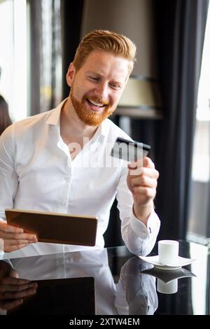 Homme d'affaires beau réussi tenant la carte de crédit, en utilisant la tablette numérique. Concept d'achat en ligne Banque D'Images