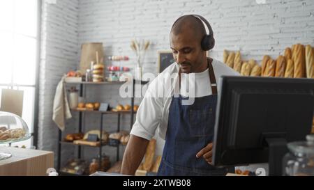 Beau jeune homme travaillant dans une boulangerie avec des étagères de pain frais en arrière-plan Banque D'Images