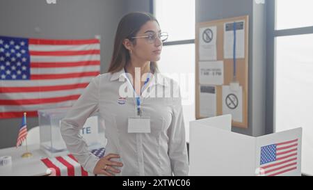 Jeune femme hispanique confiante avec l'autocollant "j'ai voté", se tient dans la salle du collège électoral américain, drapeau visible. Banque D'Images