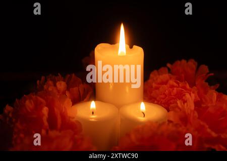 Trois bougies illuminent la scène, entourées de soucis oranges sur un jour du tissu mort. Le fond noir et la lumière des bougies créent une tradition Banque D'Images
